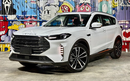 A white SUV car with a large black front grille and black multi-spoke wheels, parked in front of a colorful graffiti wall. The brand name 'JETOUR' is visible on the front grille.